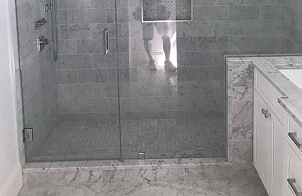 A person is standing in the shower with their reflection in it.